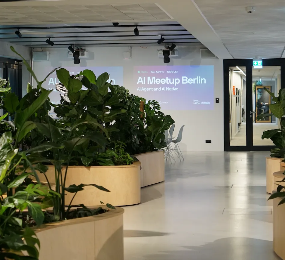 Modern indoor office space with large potted plants along a walkway and a projection on the wall announcing AI Meetup Berlin.
