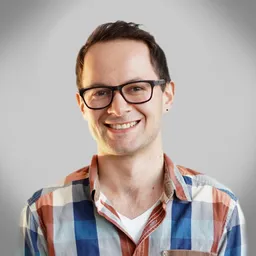 Smiling man with short dark hair, glasses, and a plaid shirt against a gray background.