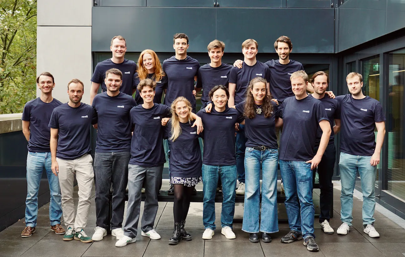 Group of 17 young adults wearing matching navy blue 'revel8' t-shirts posing outdoors in two rows.