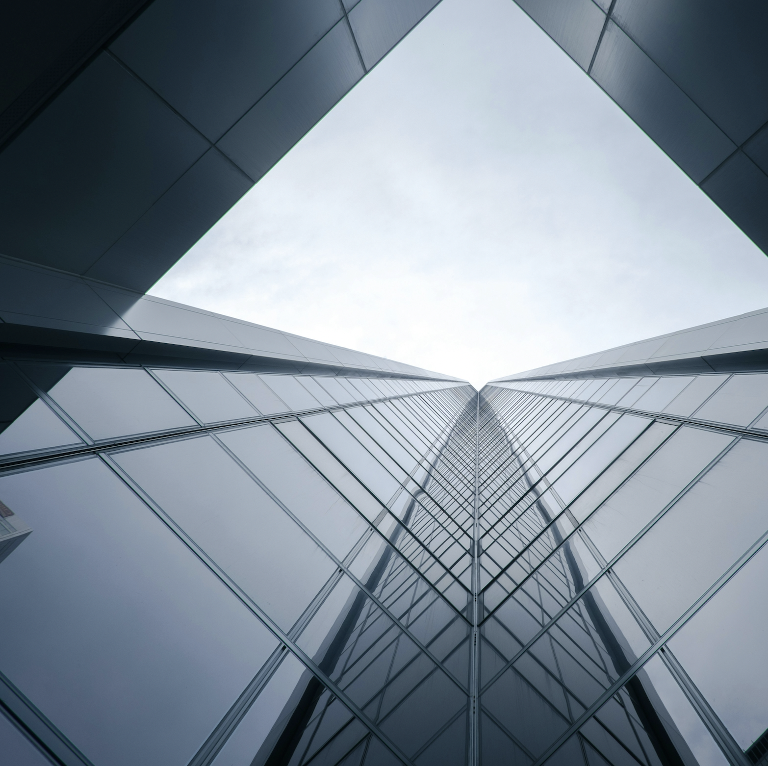Upward view of a modern glass skyscraper converging to the sky through a geometric frame.