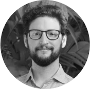 Portrait of Jules Bennett, Founder and CEO of DreamSphere, smiling and wearing glasses in front of leafy plants.