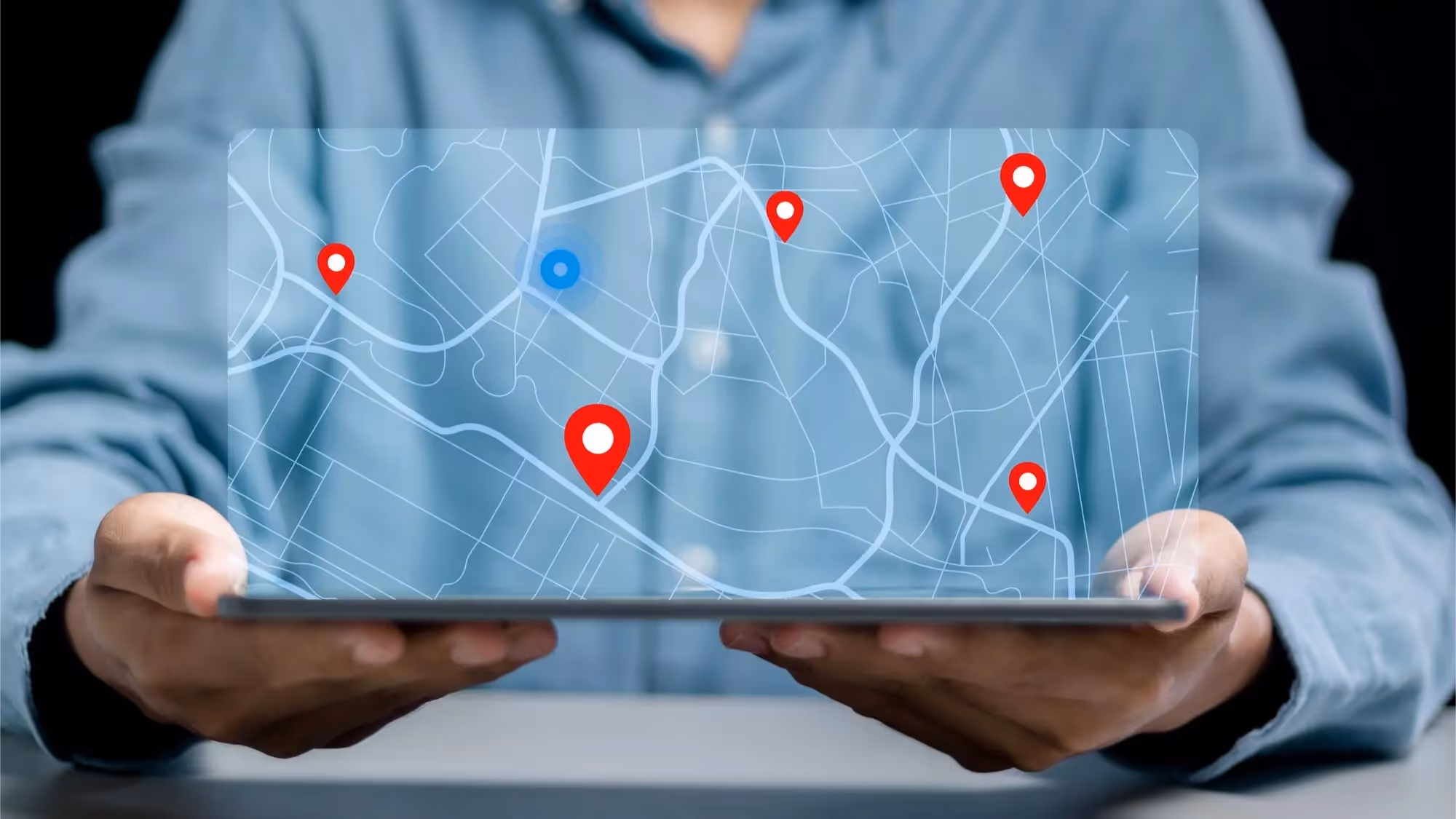 A person in a blue shirt holds a tablet displaying a digital map with several red location pins and one blue pin. The floating interface suggests cloud-based retail communications supporting location tracking across retail outlets. It emphasizes streamlined communications for small business logistics.