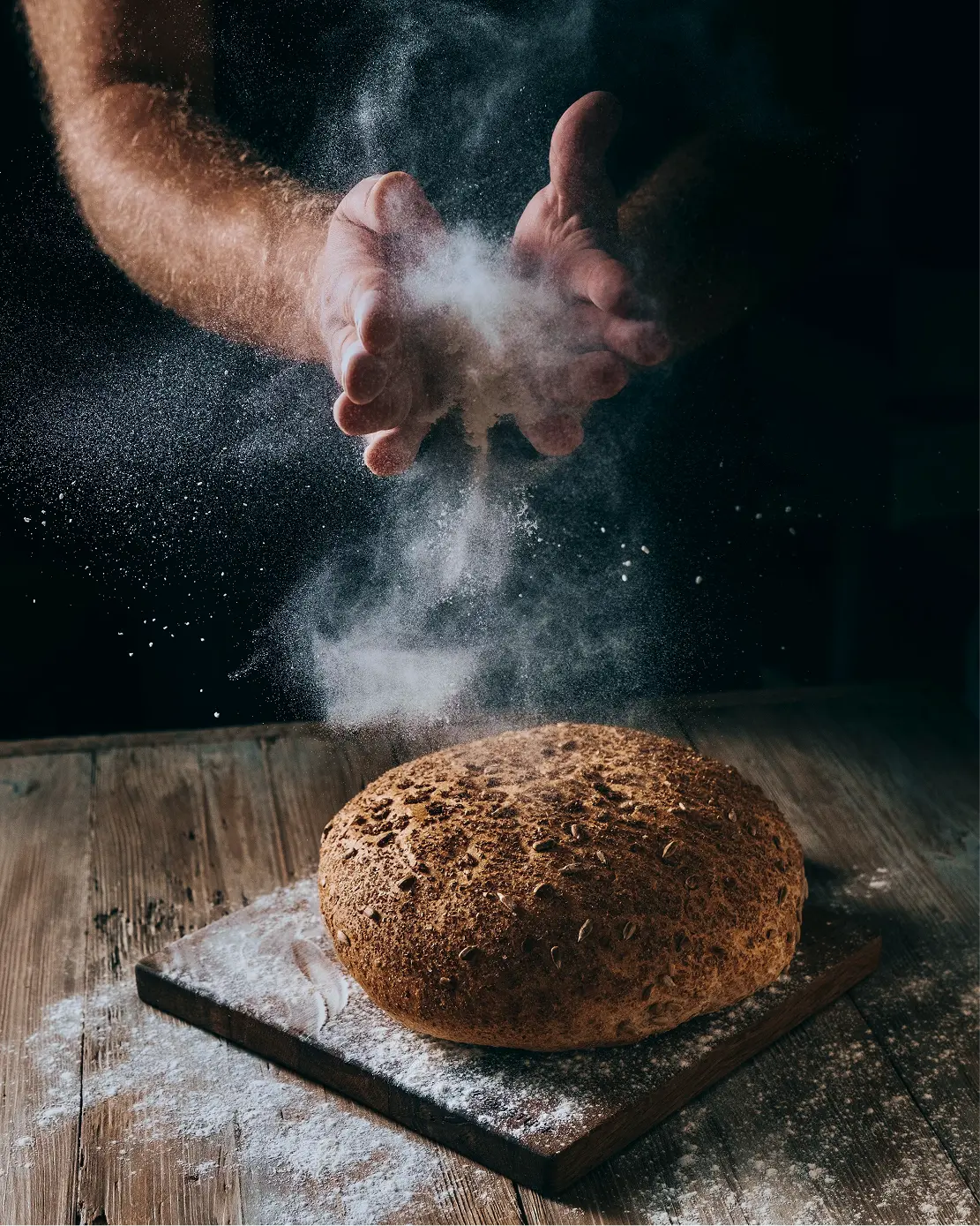 A baker's hands spreading flour over a loaf of artisanal bread