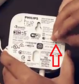 Bottom view of Philips Hue Bridge, with paperclip pressing reset button.