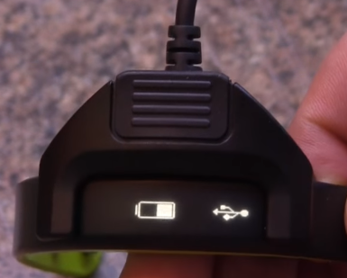 Garmin Vivosmart physically connected with the supplied charging cable, displaying the battery and USB icons.