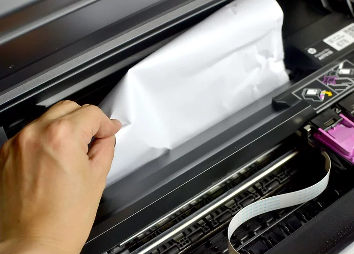 Photo of jammed paper being removed from the inside of a printer.