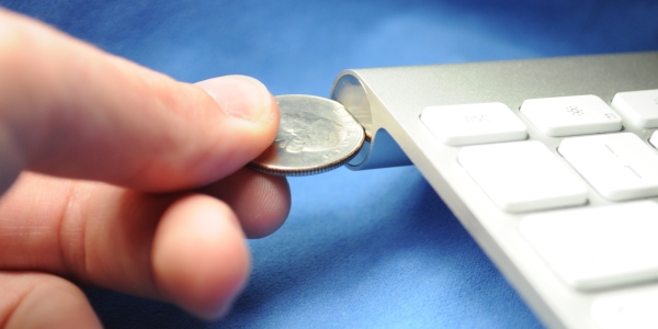 Using a coin to open the battery compartment cover of an Apple Wireless Keyboard.