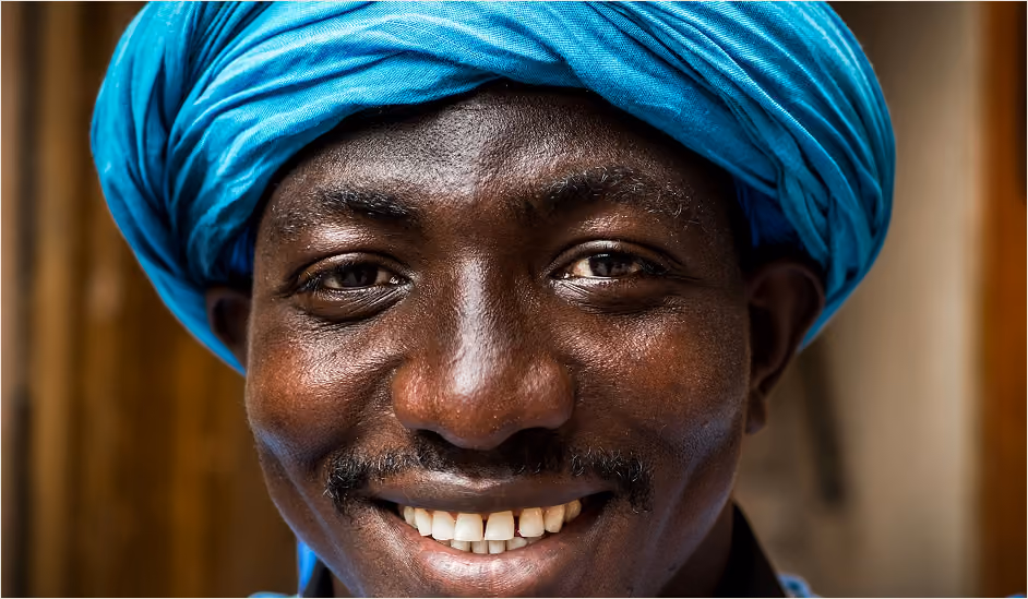 Close-up of a smiling man wearing a bright blue turban and a mustache.