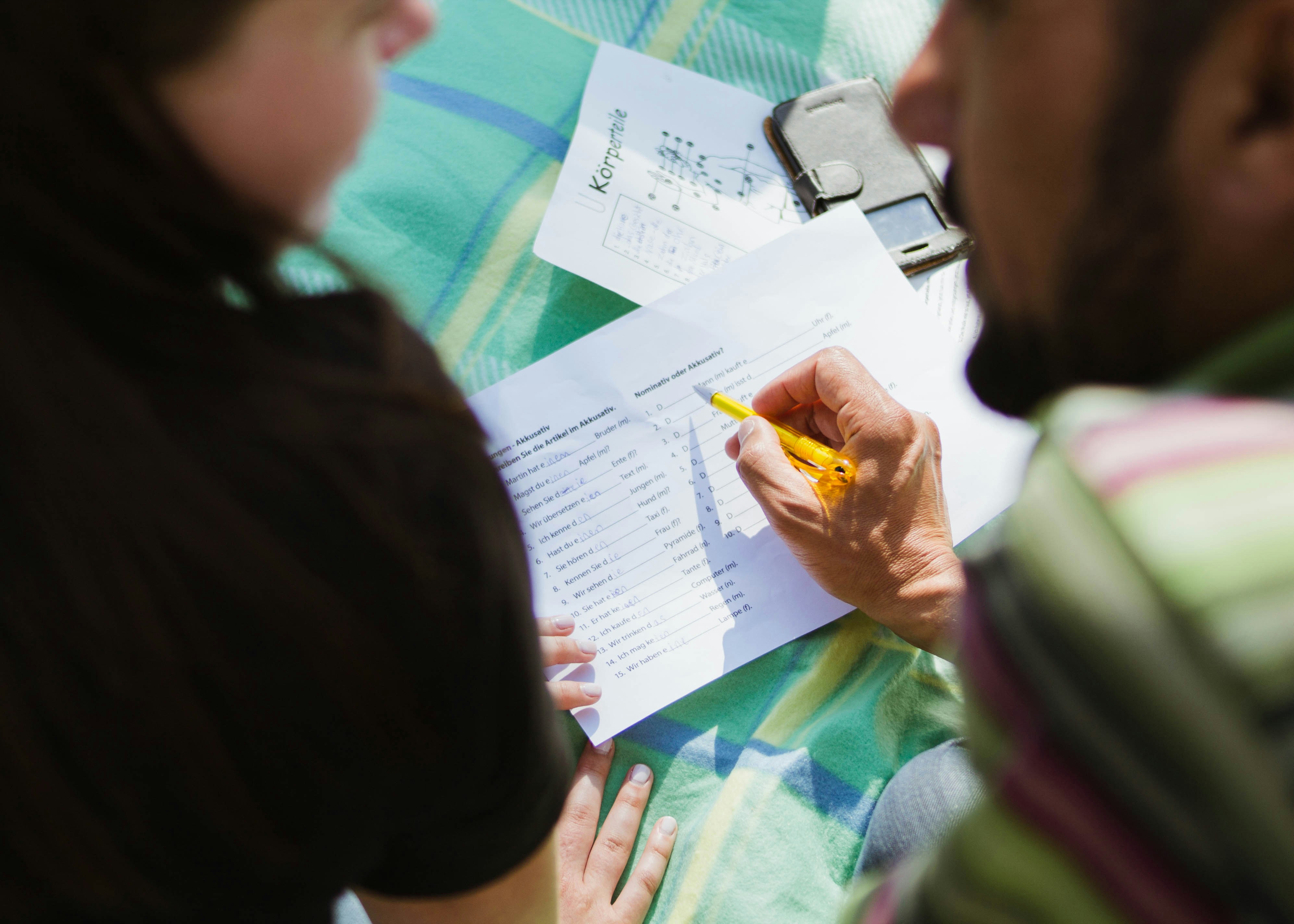 A teacher and student review a worksheet together, with the teacher pointing at a question with a pencil.