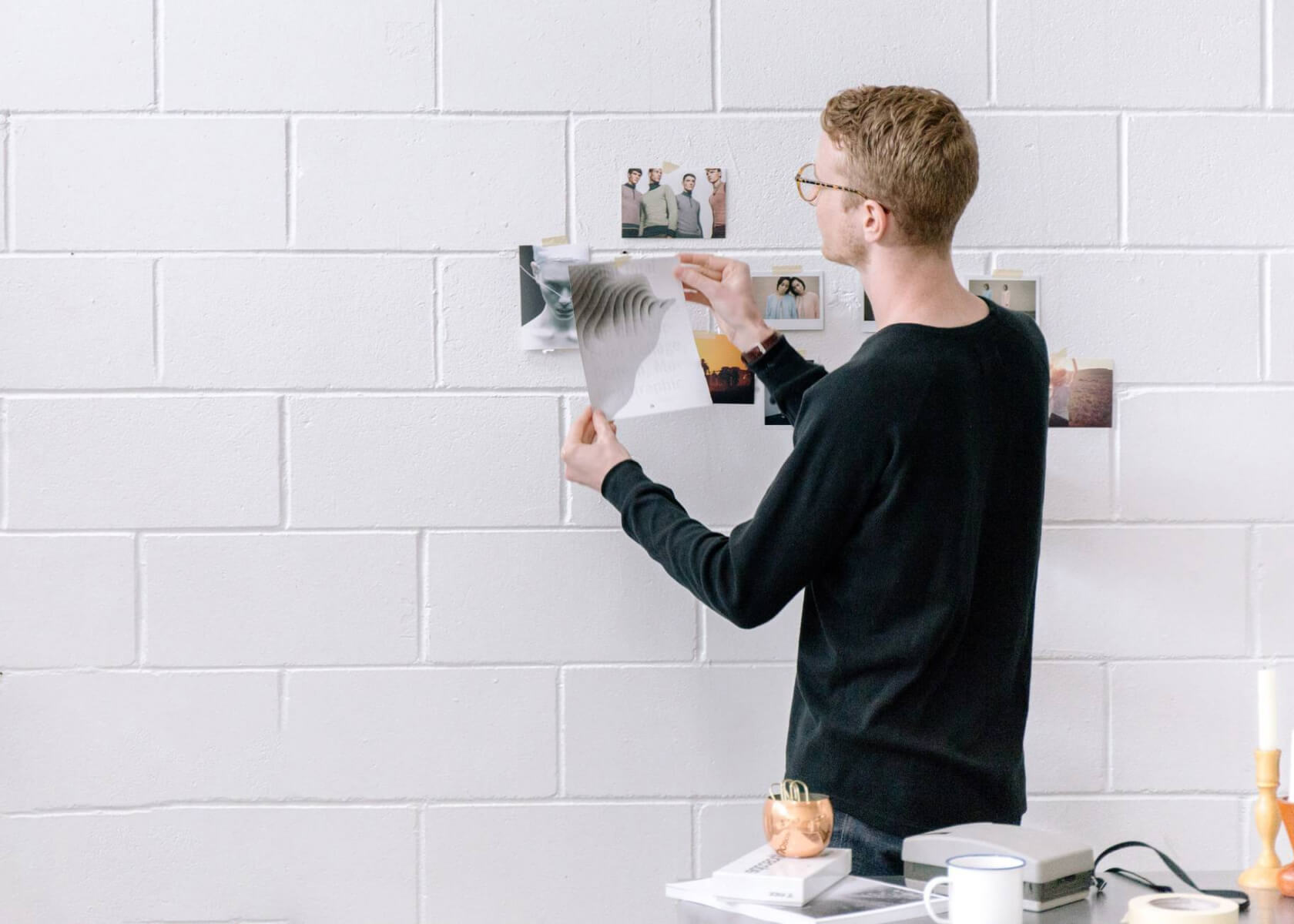A man places photographs up on a brick wall in an office setting.