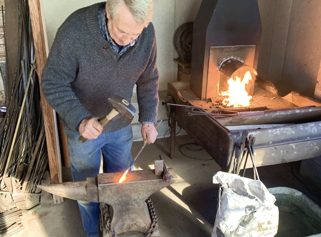 An image of a workshop participant working at the anvil in the blacksmith shop.