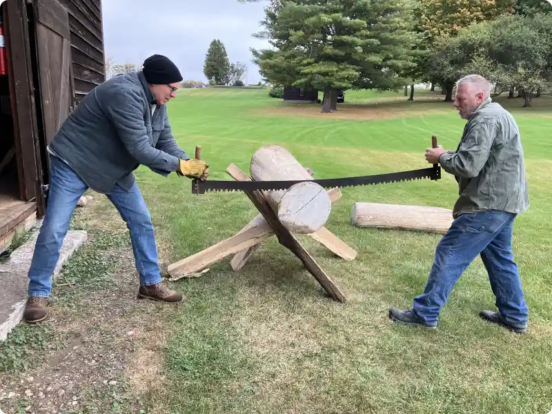 A picture of two men on an old long saw cutting the end off of a log.