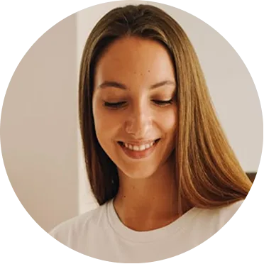 Smiling young woman with long brown hair looking downward, wearing a white shirt.