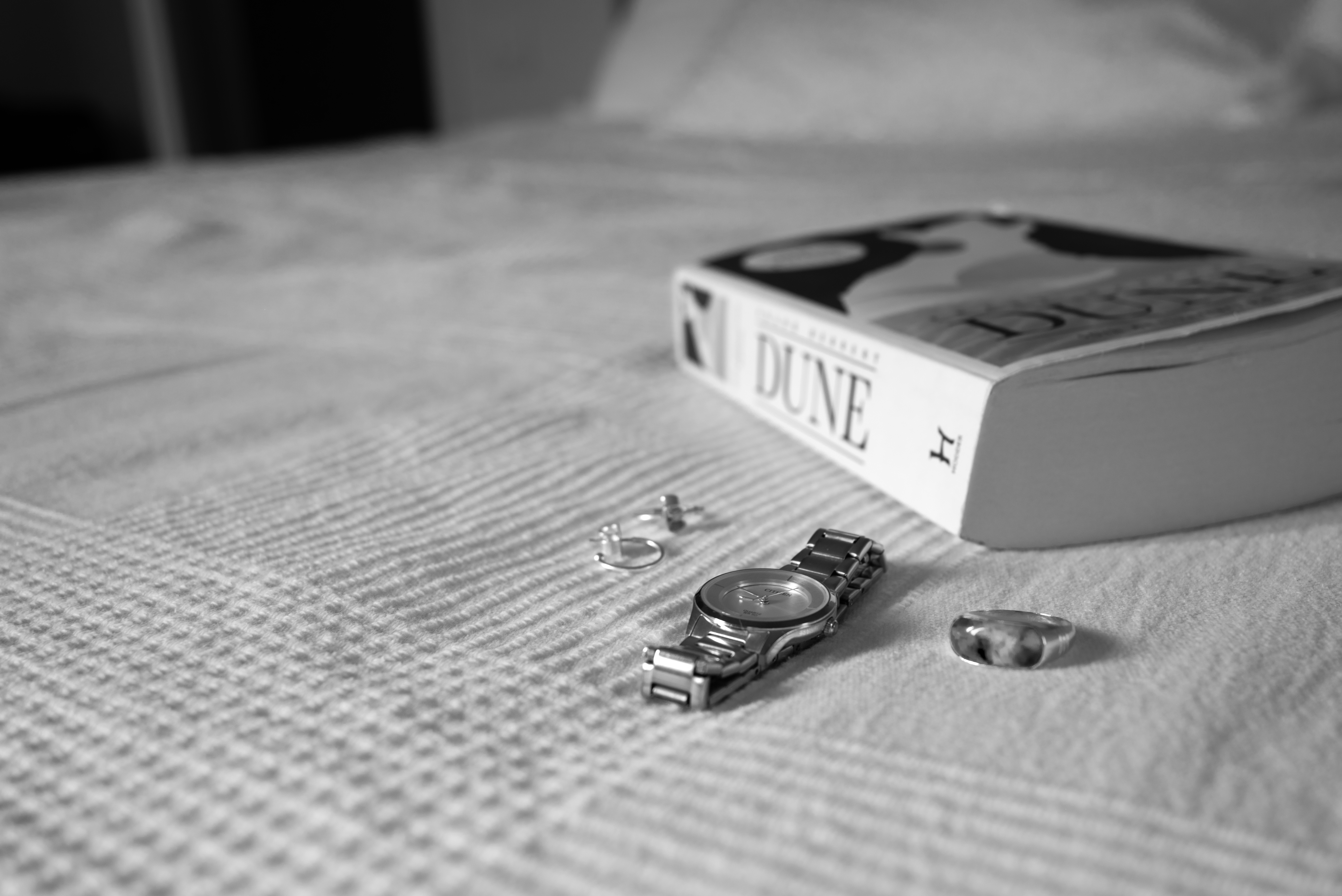 Black and White image: Watch, jewellery and book on bed