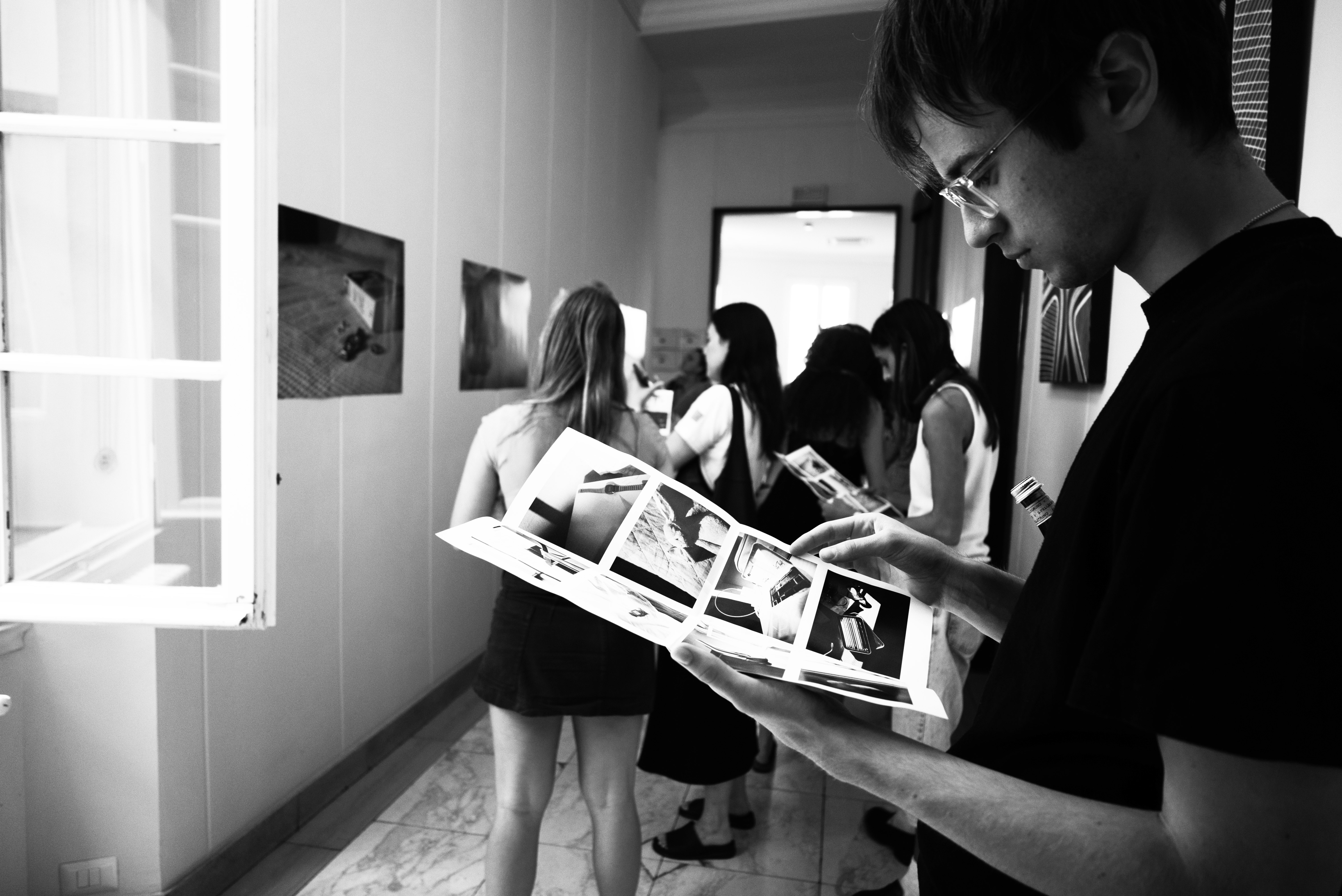 Black and White image: Hallway with photographs and person reading brochure