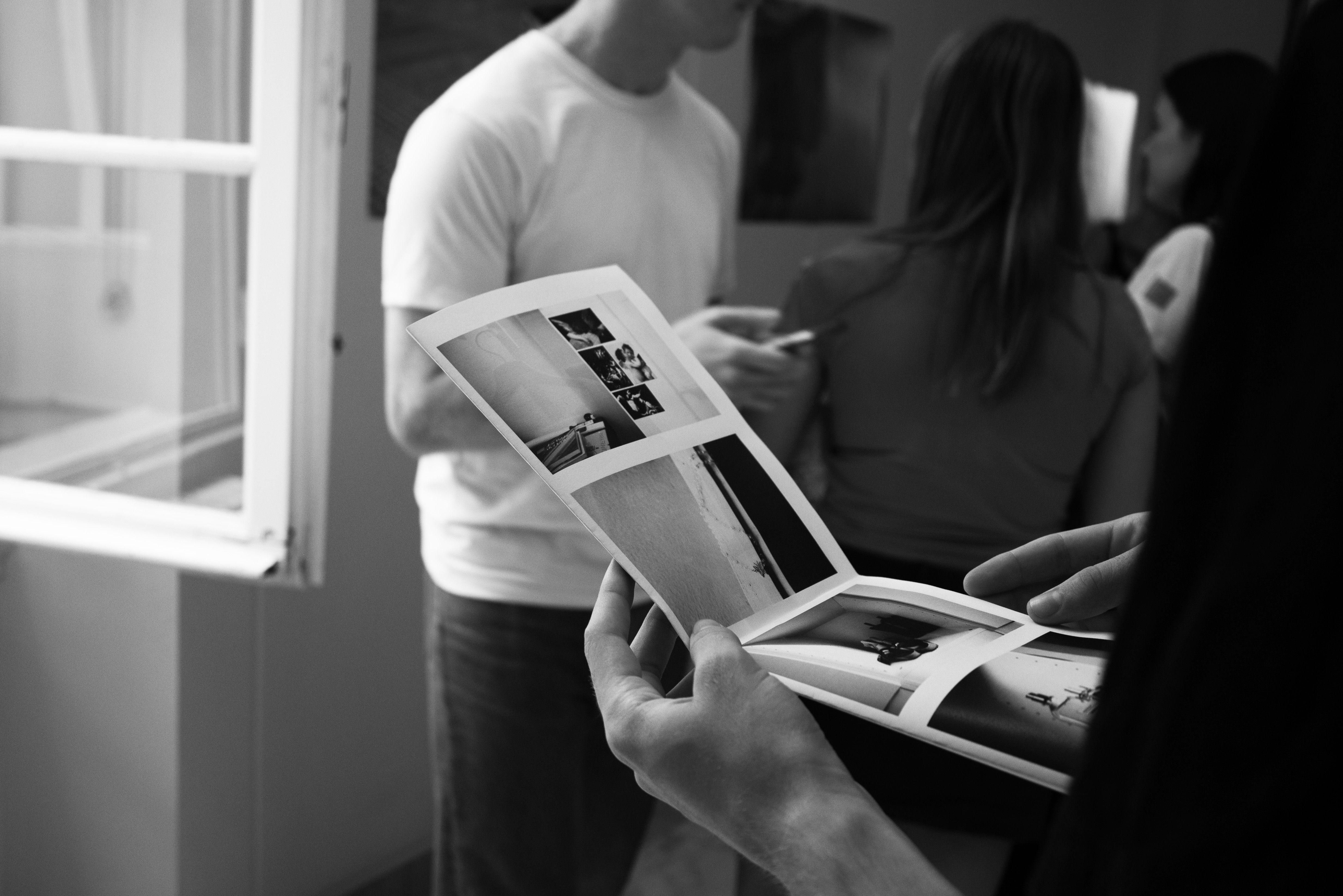 Black and White image: Hallway with photographs and person holding brochure