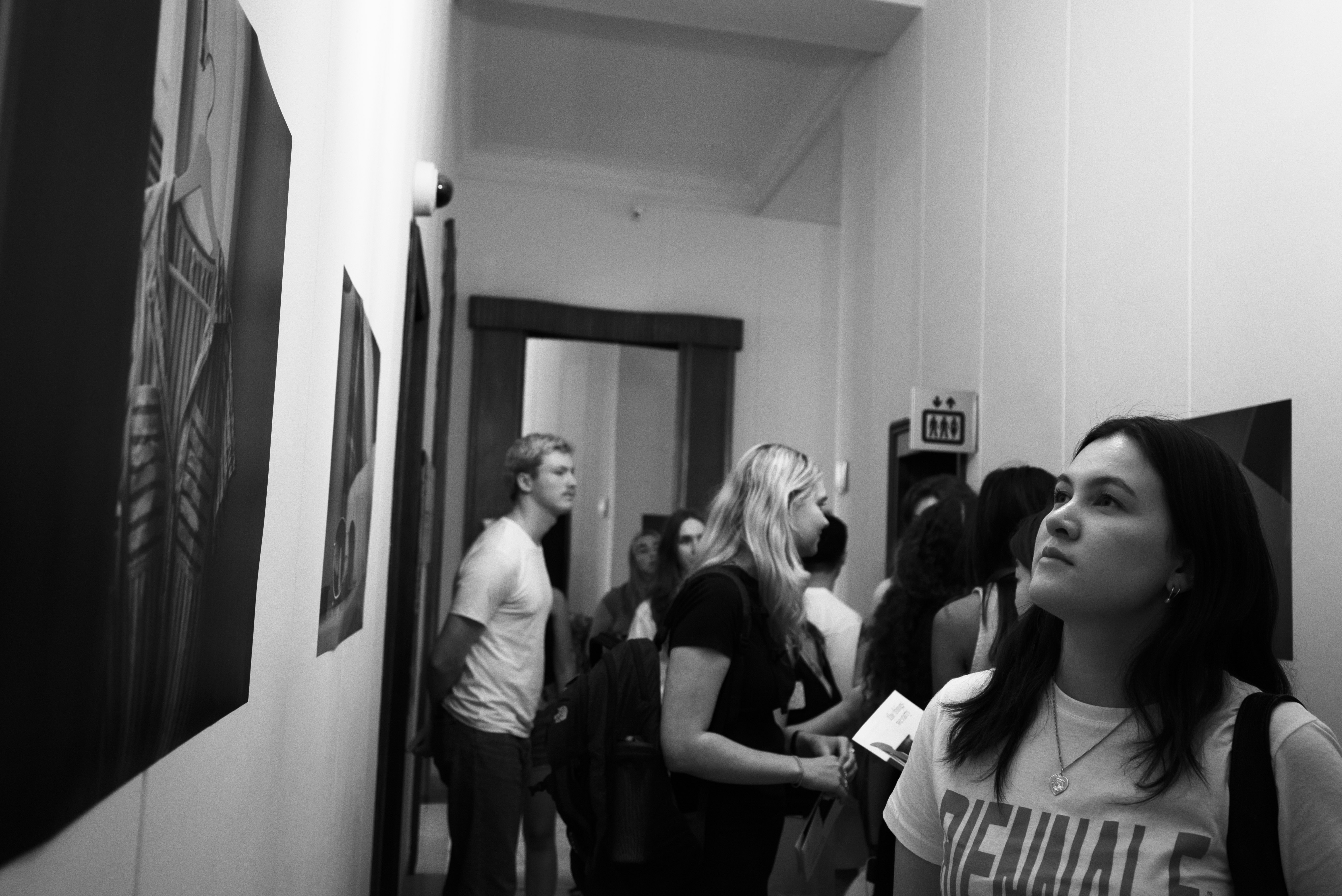 Black and White image: Hallway with photographs and people