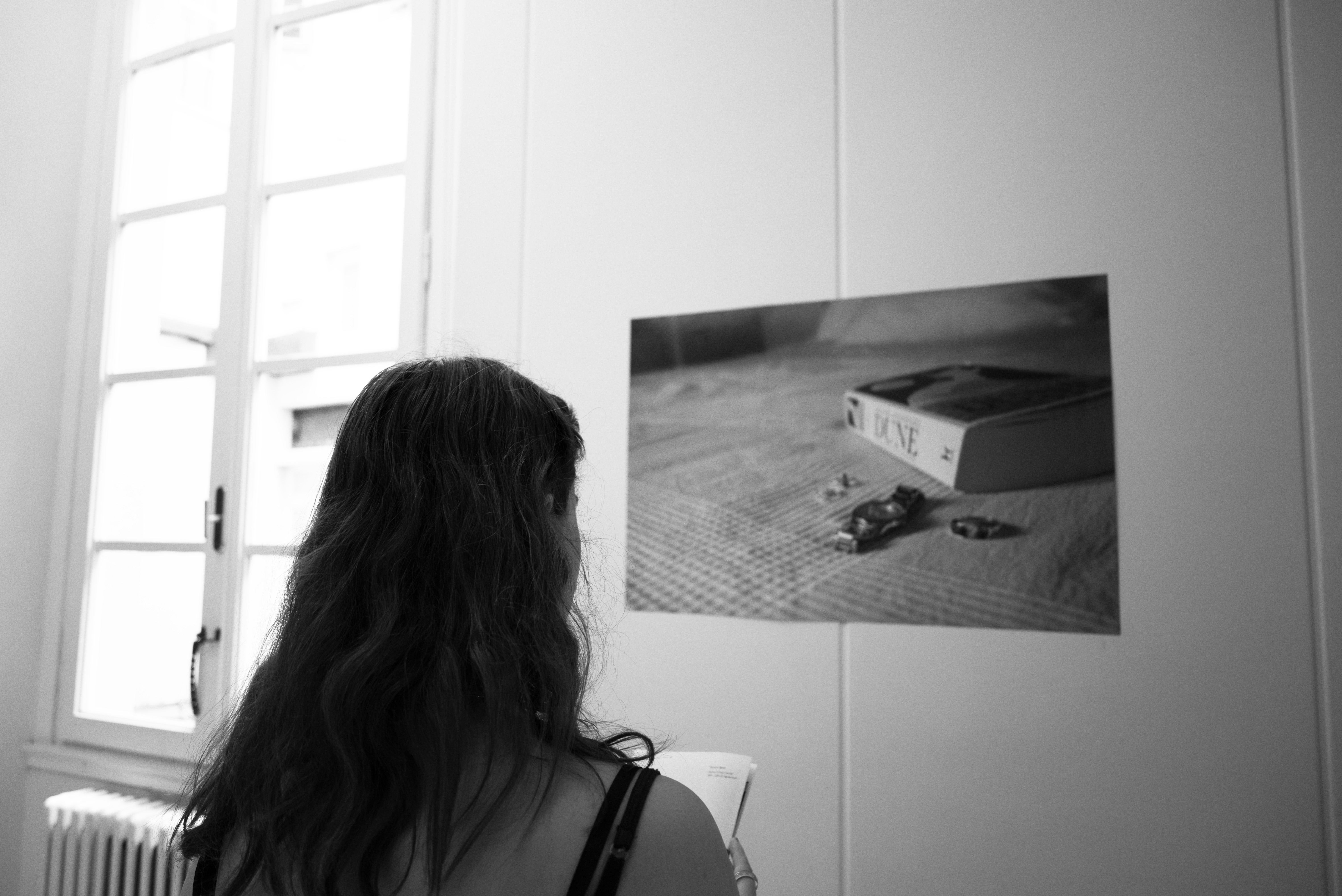 Black and White image: Hallway with photographs and person looking at photograph