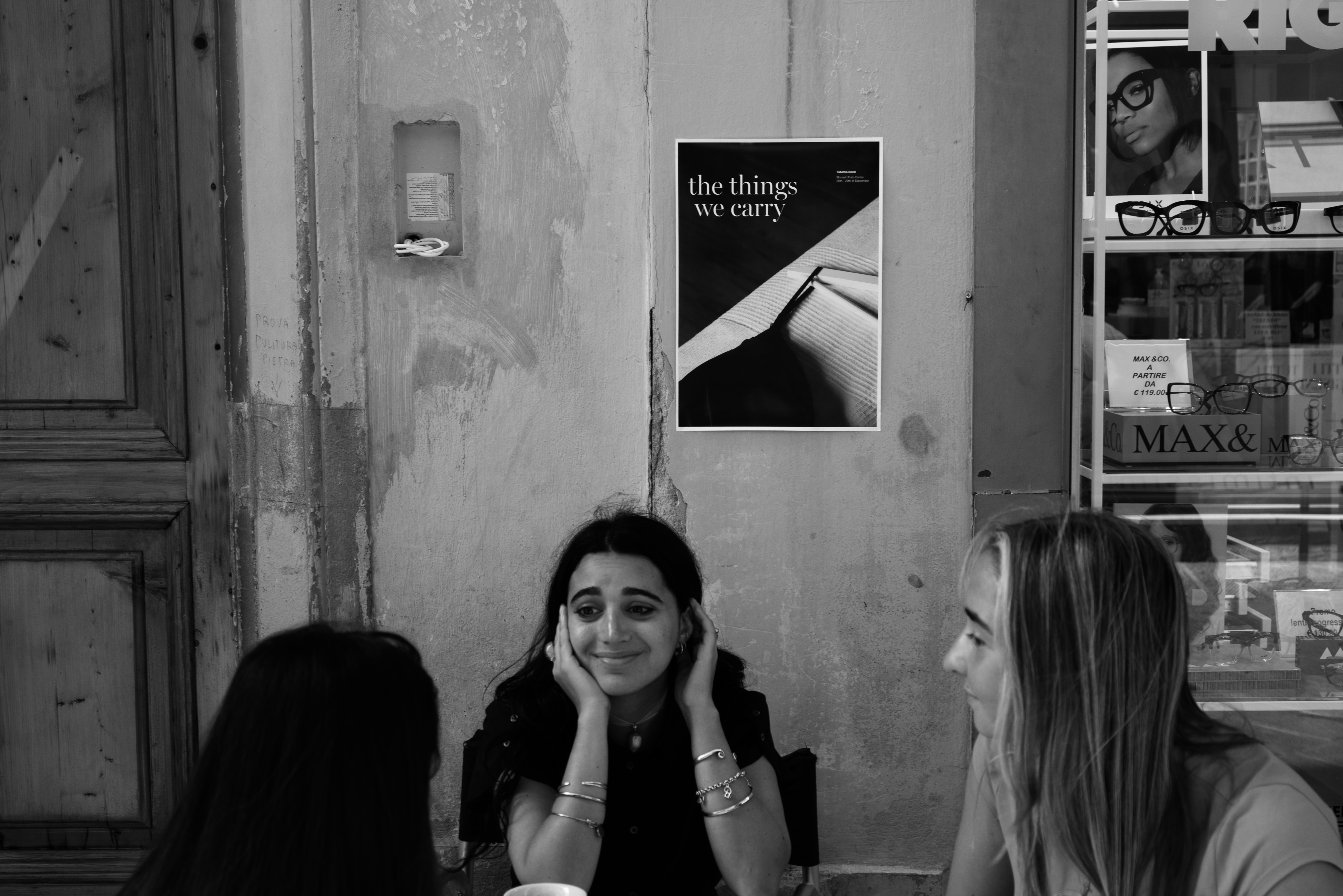 Black and White image: Poster on wall above girls talking