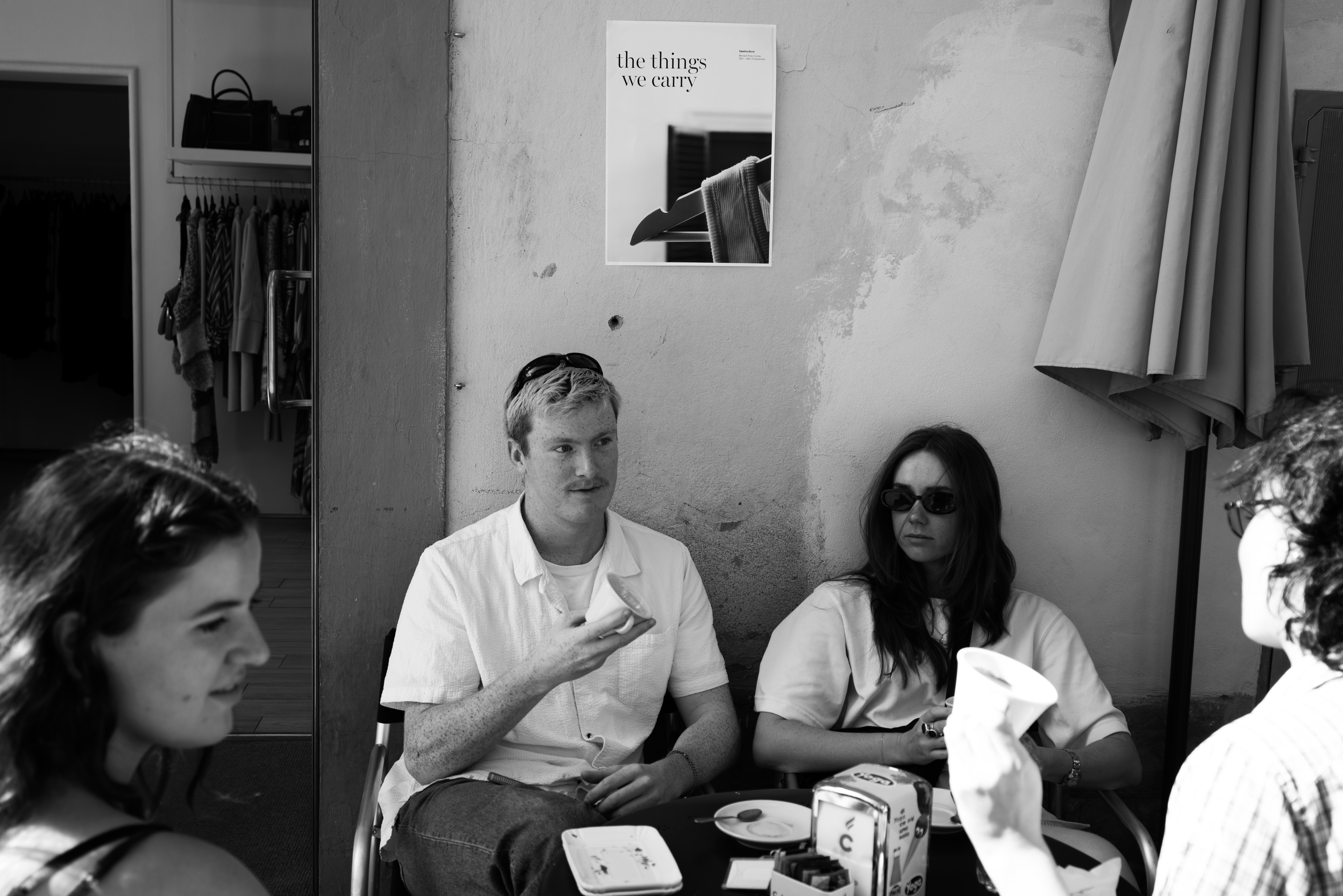 Black and White image: Poster on wall and people drinking coffee