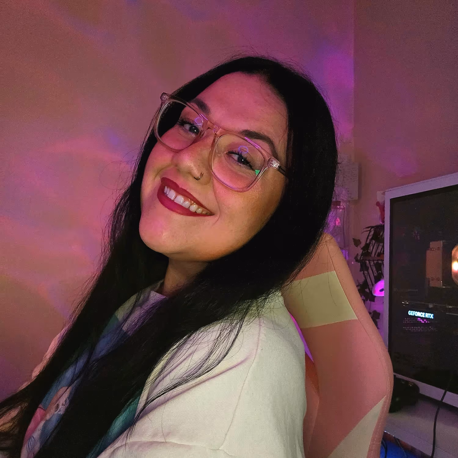Smiling woman with long dark hair and glasses, sitting in a room with purple lighting.