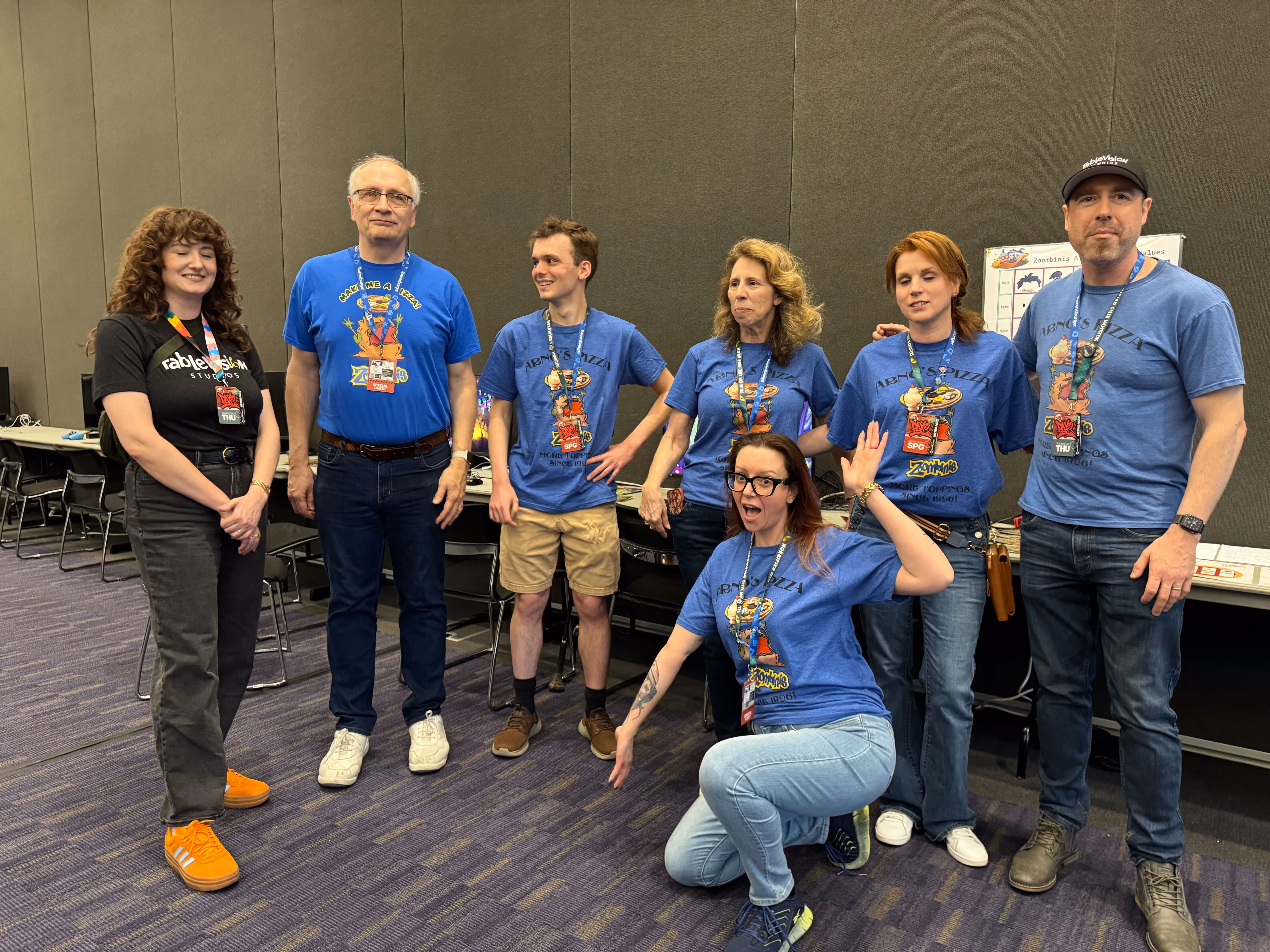 Group of seven people wearing Zoombinis-themed shirts posing together in a convention setting.