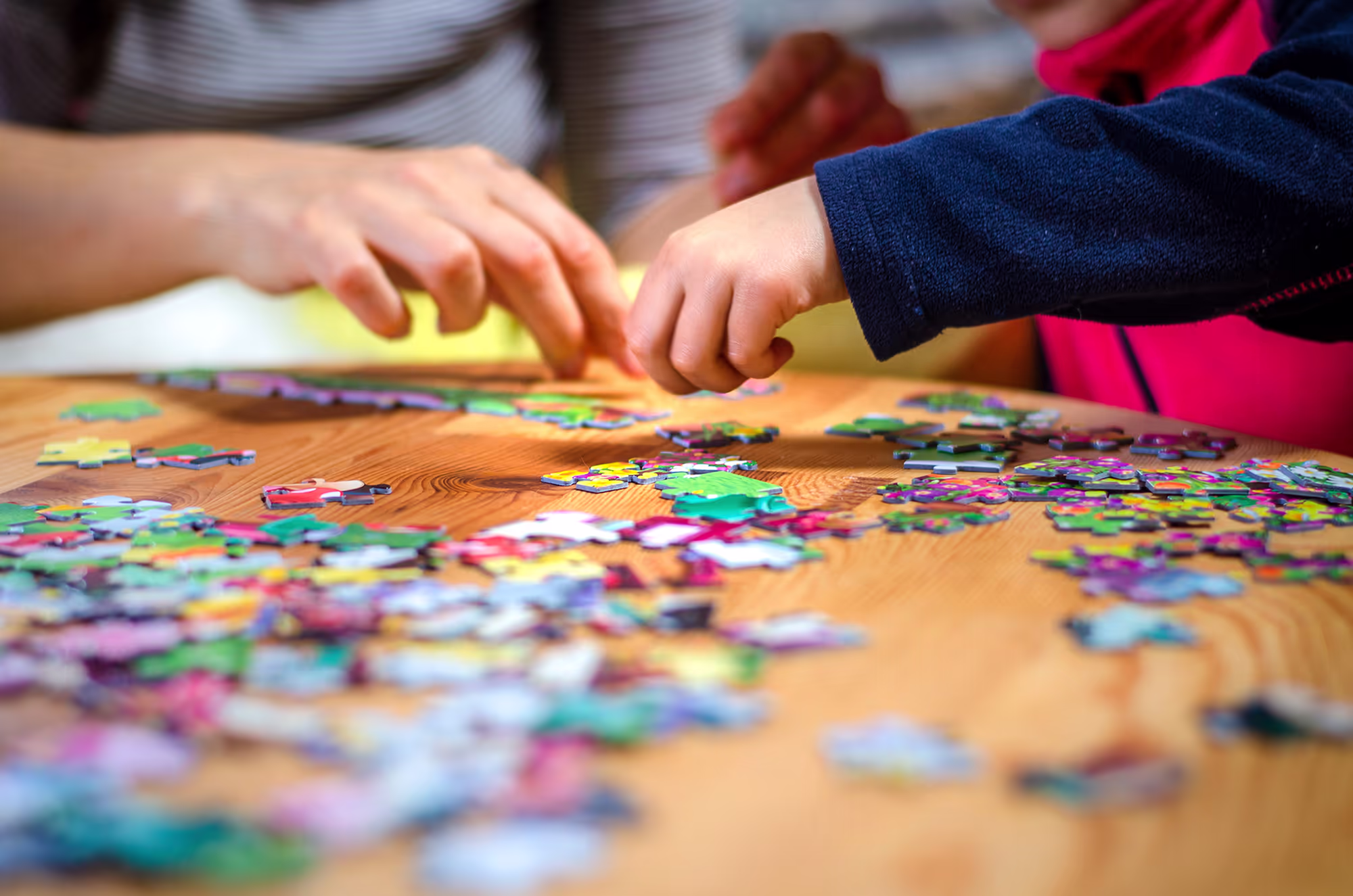 Close-up of two people’s hands working together on a colorful jigsaw puzzle on a wooden table.