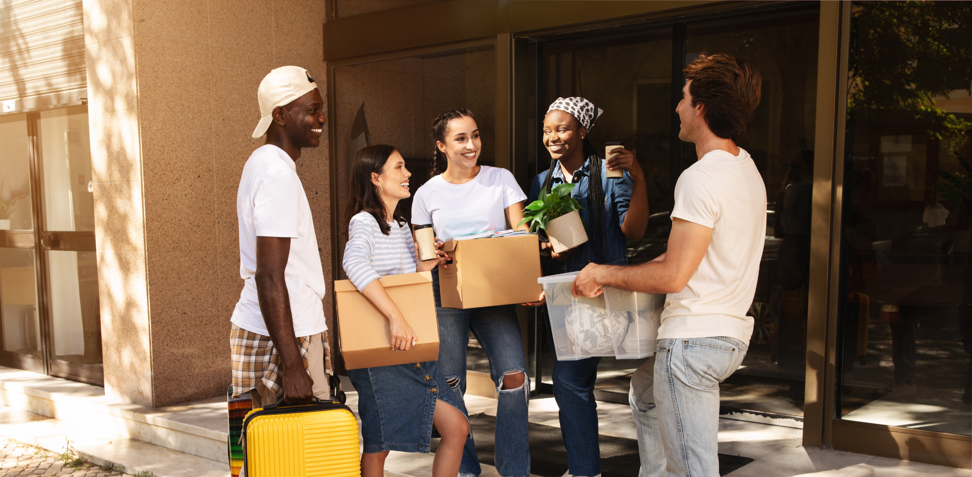 Four disabled people of color gather around a table during a meeting. A Black woman sitting on a couch gestures and speaks while the three others (a South Asian person sitting in a wheelchair, a Black non-binary person sitting in a chair, and a Black non-binary person standing with a clipboard and cane) face her and listen.