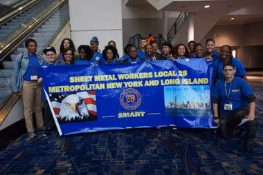Group of SMART Local 28 members standing together indoors, holding a banner for Sheet Metal Workers Local 28 Metropolitan New York and Long Island.