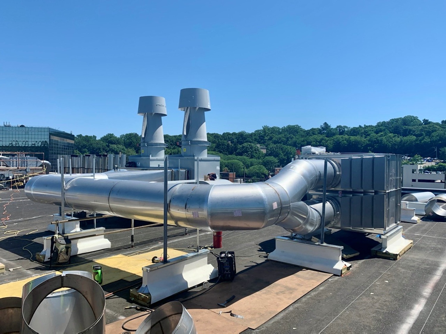 Industrial rooftop ventilation system with large round metal ducts and two vertical exhaust fans under clear blue sky.