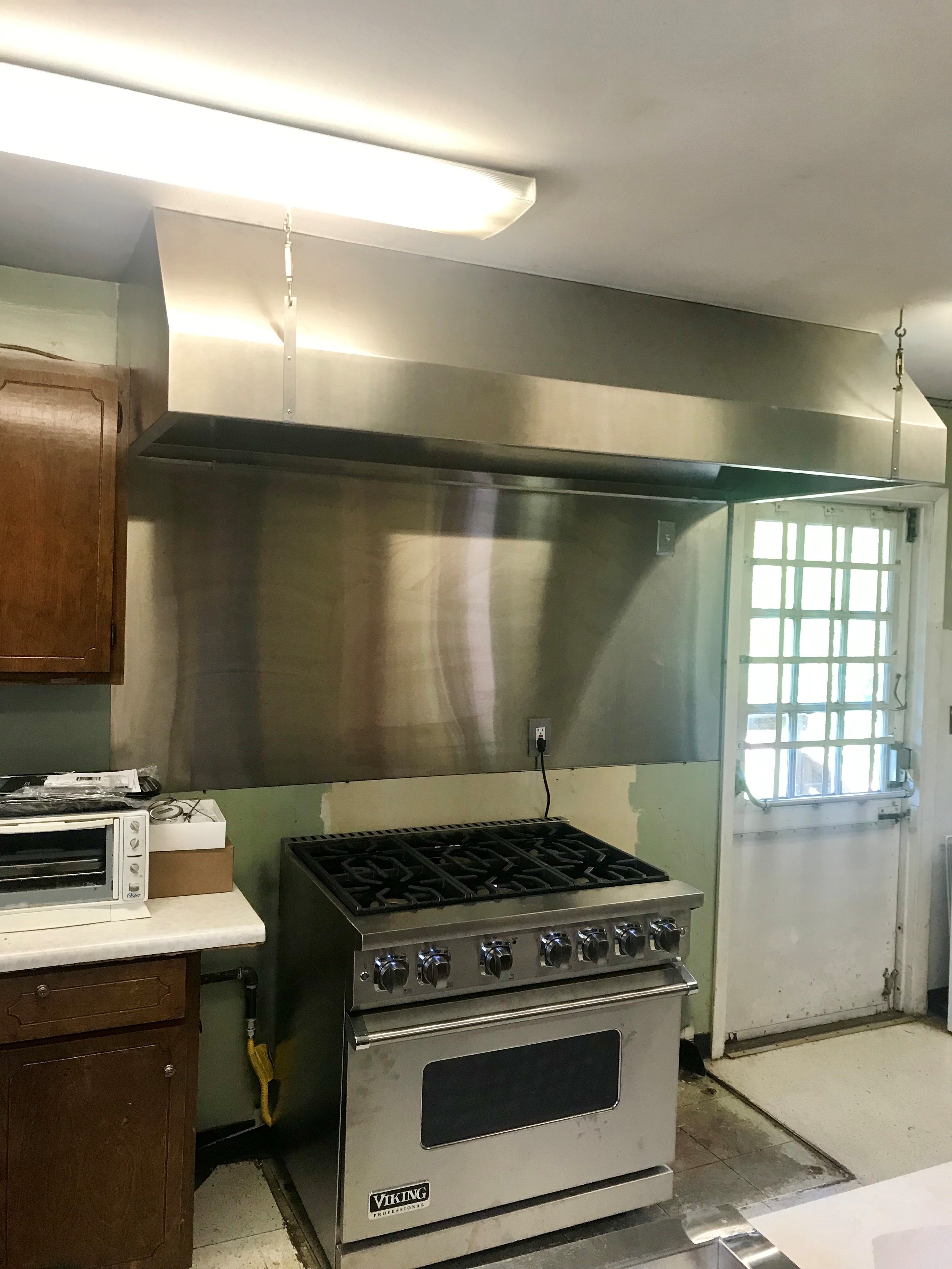 Professional Viking stainless steel gas stove with six burners under a large stainless steel kitchen hood.