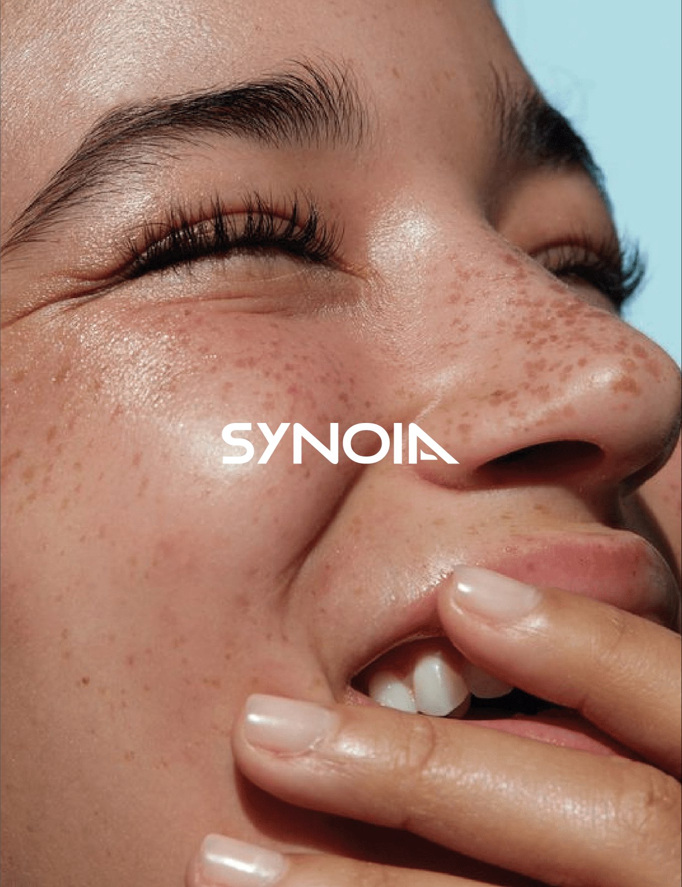 Close-up of smiling woman with freckles and Synoia Technologies skincare logo, representing natural and adaptive skincare branding by Studio Wisdom.