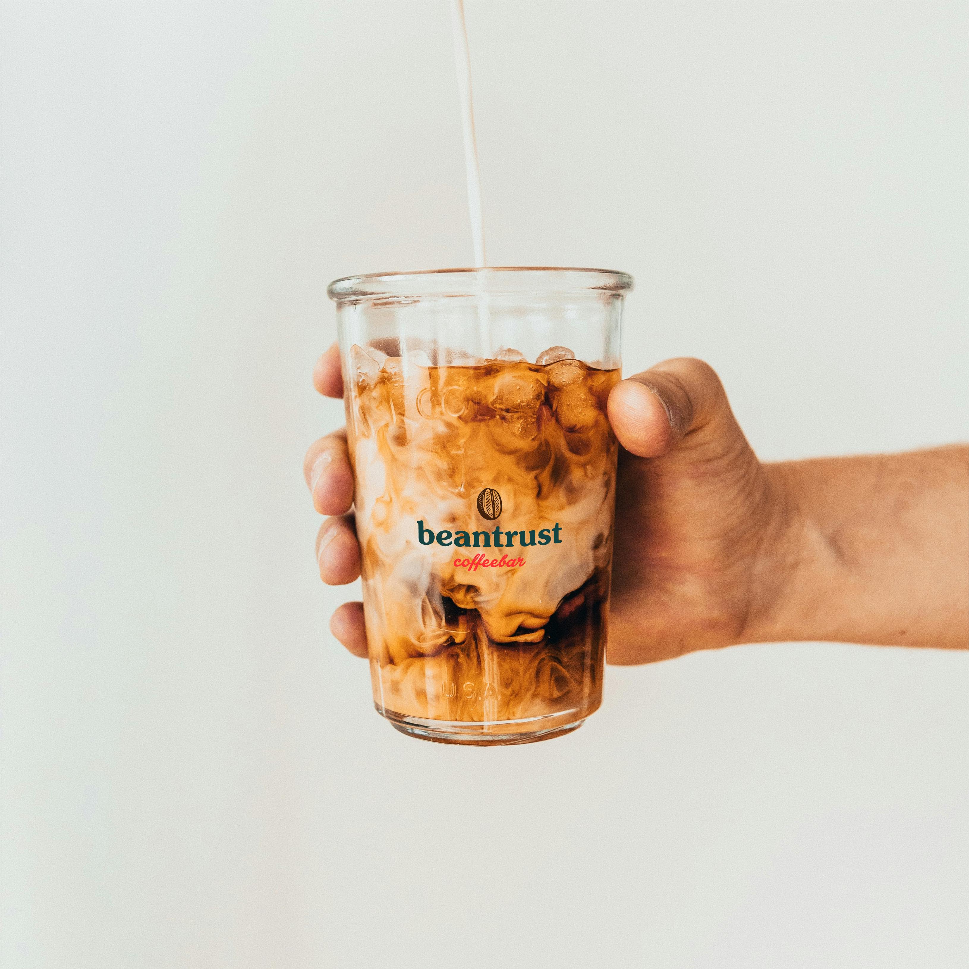 Studio Wisdom’s branded glassware for Beantrust, showcasing a milk swirl and the coffee bar’s logo on iced coffee