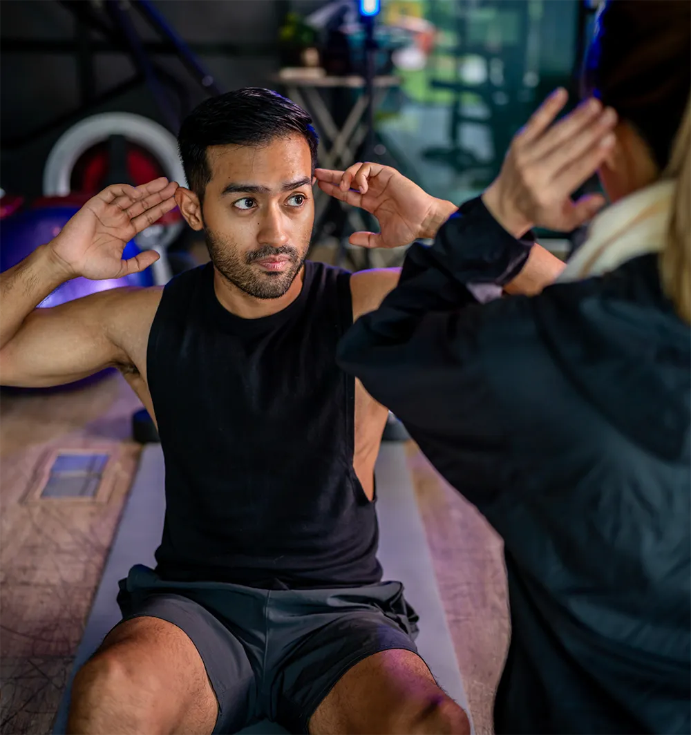Man performing sit-ups on a gym mat with a personal trainer guiding him during a workout session.