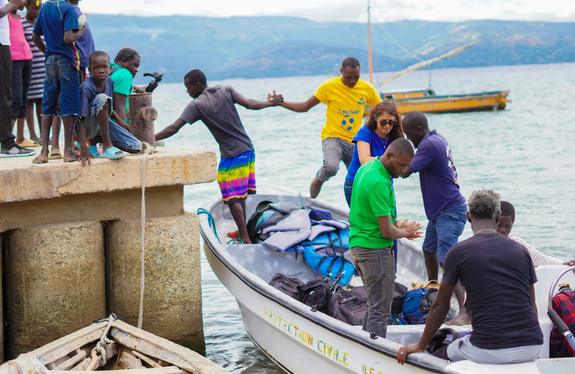 Des hommes et une femme aident des gens à descendre d'un bateau proche d'un quai sur une étendue d'eau.