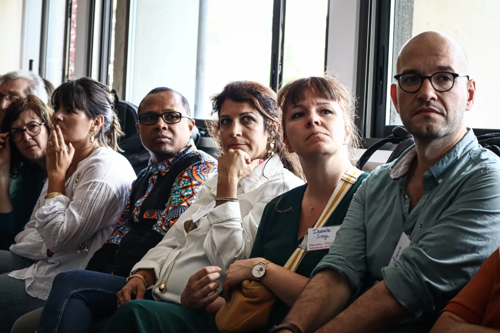 Un groupe de personnes assises, attentives, lors d'une réunion ou conférence en intérieur.