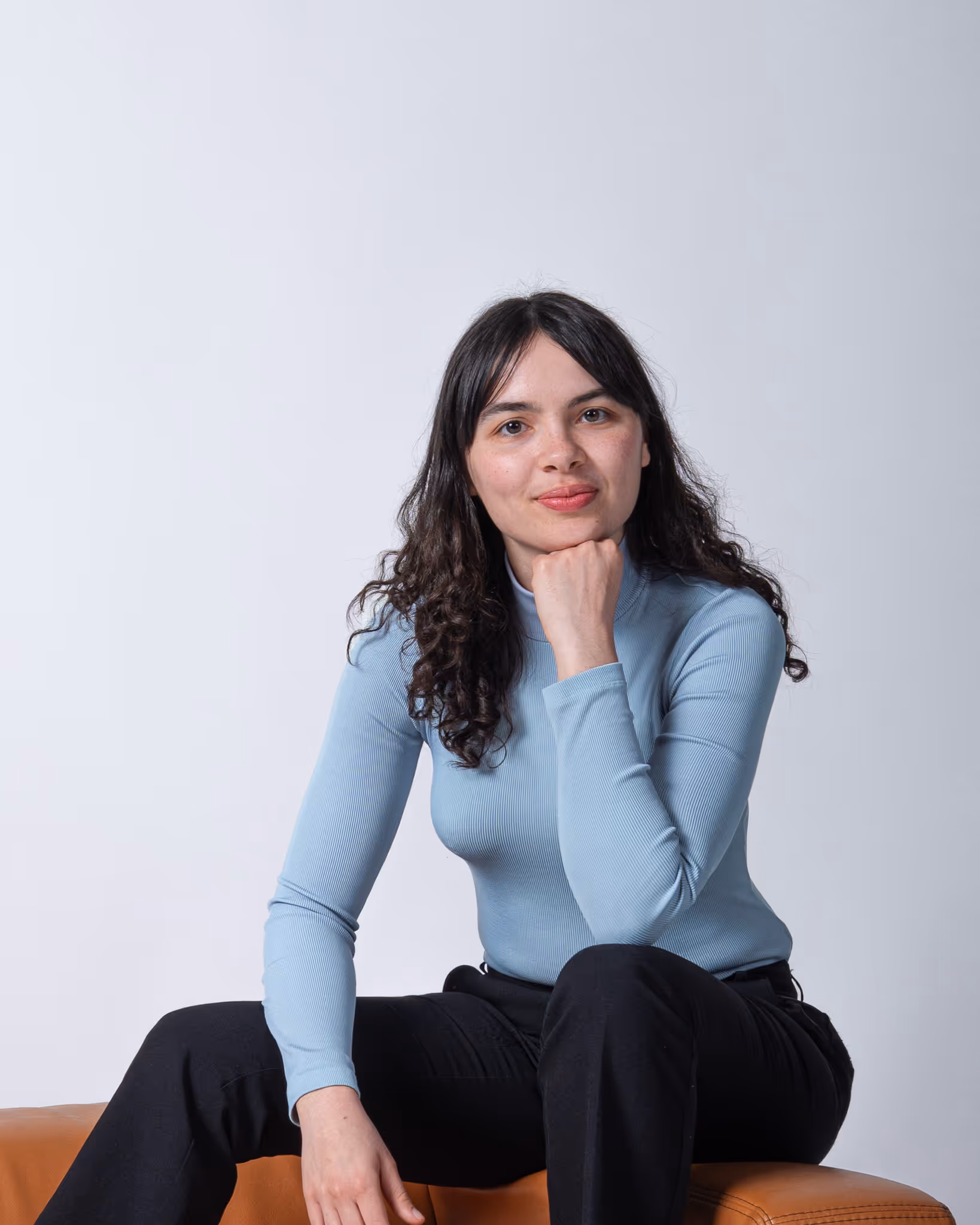 Portrait in einem Fotostudio von einer Person, die auf einem braunen Ledersofa sitzt 