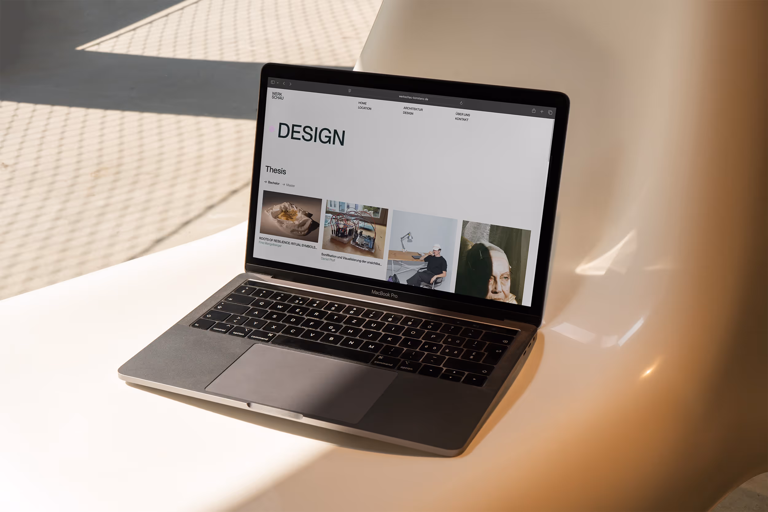 Design Seite von der Werkschau auf einem Laptop, der auf einem beigenen Stuhl liegt, im Hintergrund eine Straße