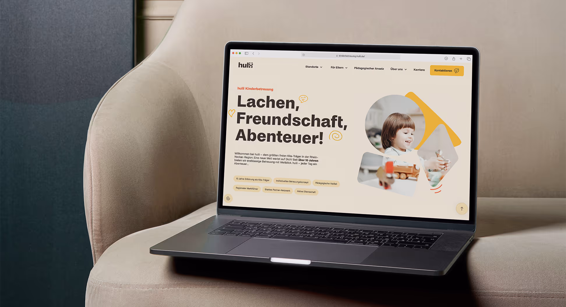 Hulii Website, auf der steht "Lachen, Freundschaft, Abenteuer!", PC der auf einer beigen Couch steht