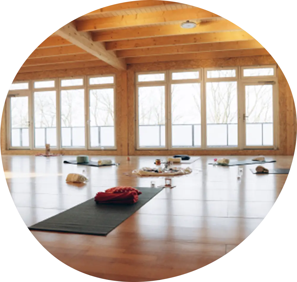 Geräumiges Yogastudio mit kreisförmig angeordneten Matten, Kissen und Decken auf einem Holzboden.
