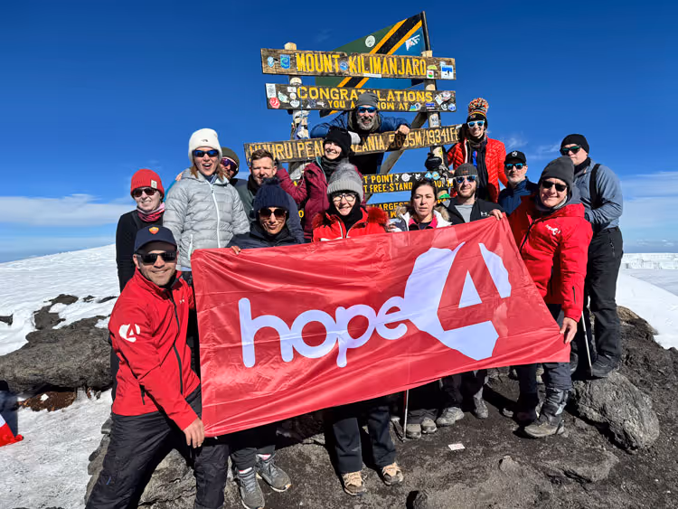 A group of hikers celebrate reaching the peak of mount Kilimanjaro on an Uncharted Summits trek.