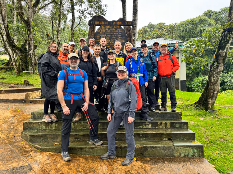A group of climbers poses with the sign at the Machame Gate, mount Kilimanjaro.