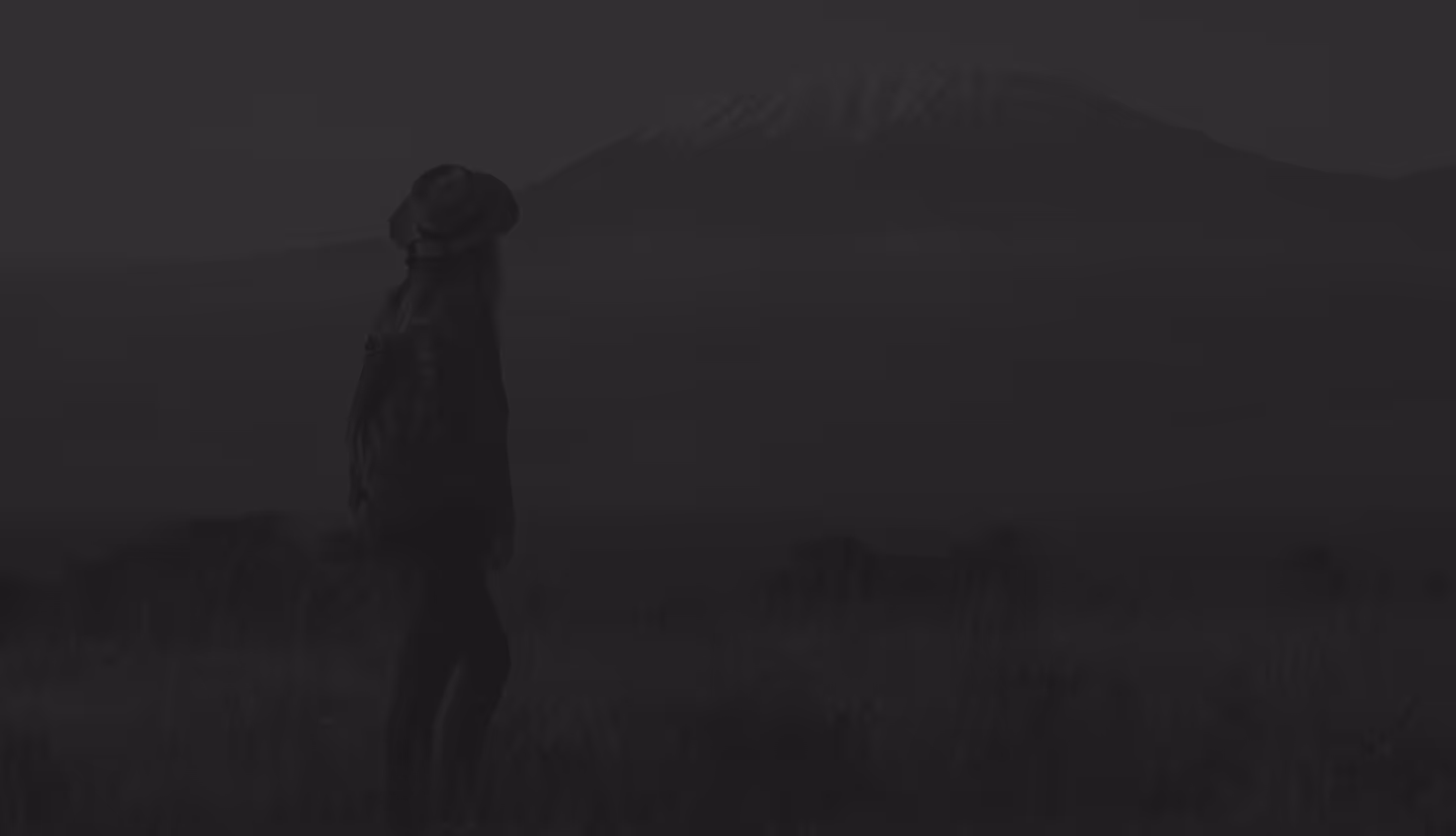 A faded image of a climber looking at Kilimanjaro