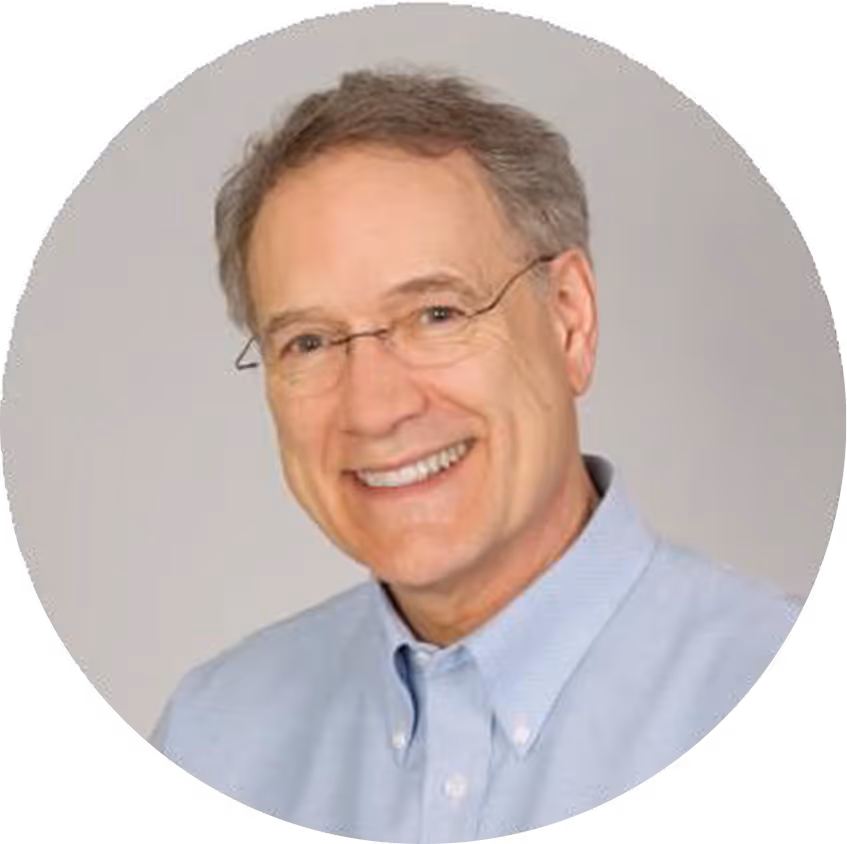A man wearing glasses and a blue shirt smiles for the camera.