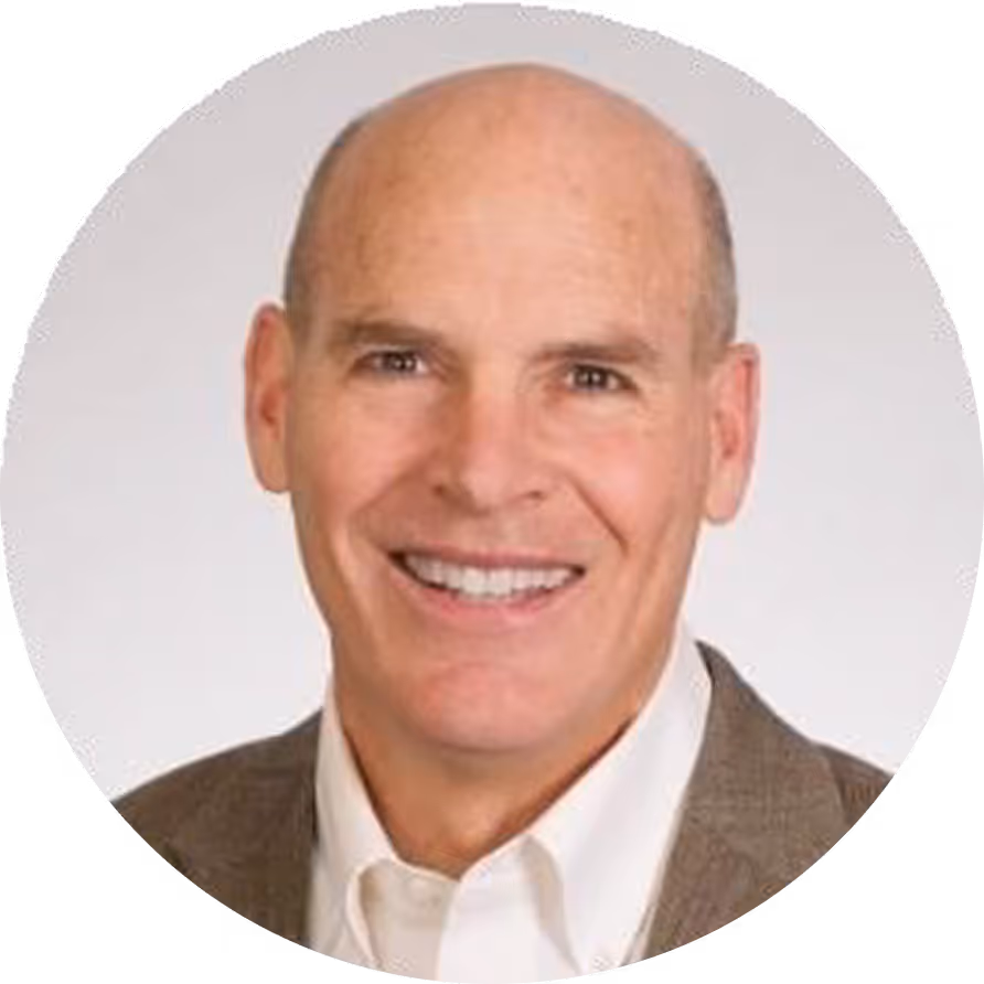 A man with a white shirt and a brown jacket smiling.