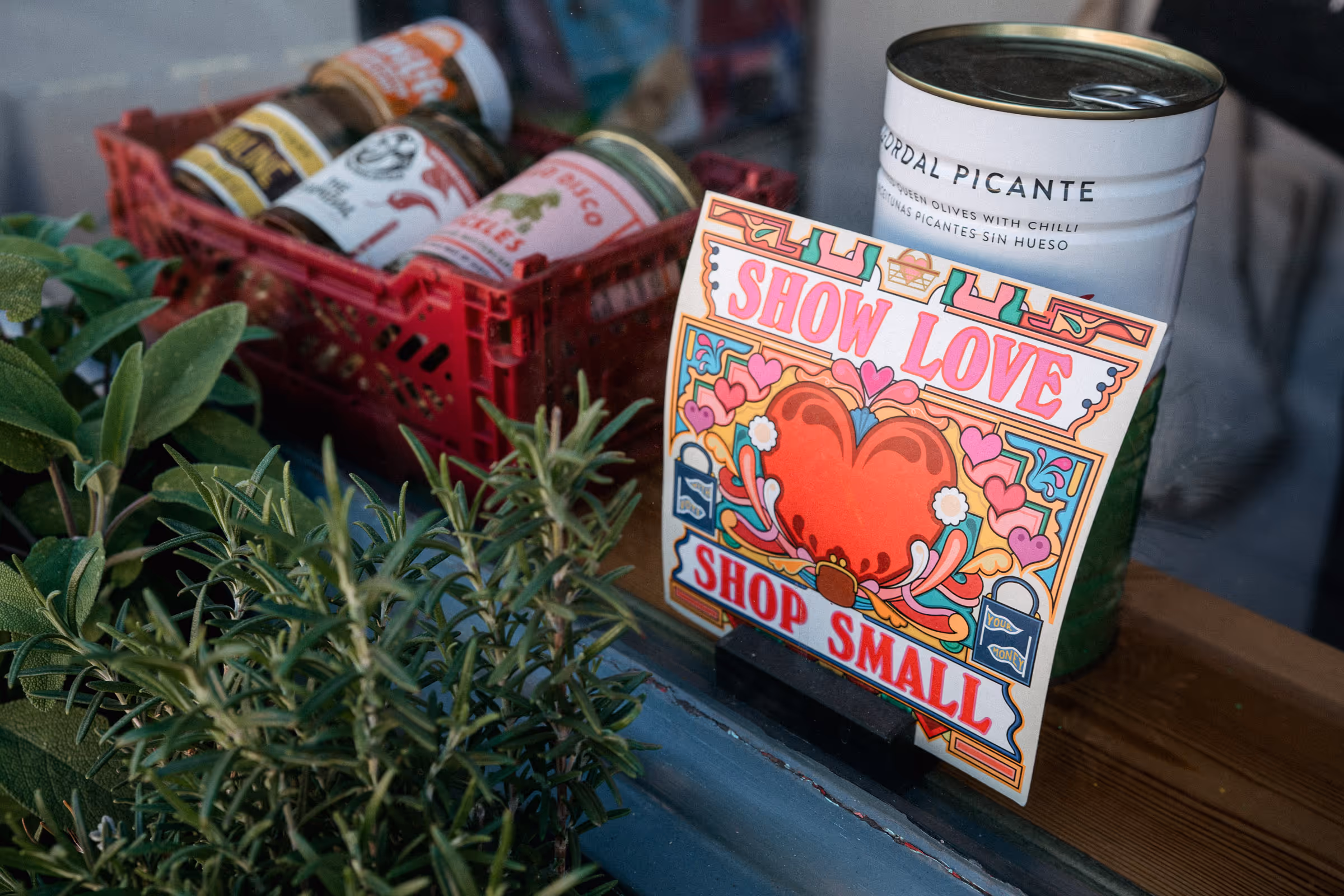 "Show Love, Shop Small" sign in Deli window with fresh herbs growing
