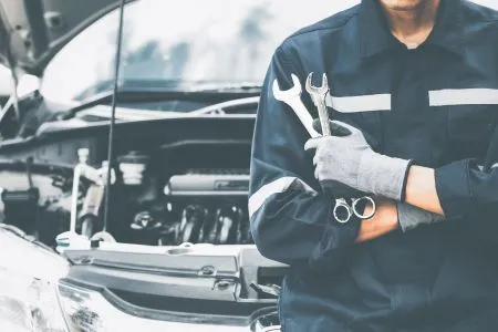Transmission needs repair shown with a mechanic in uniform holding wrenches near an open car hood.