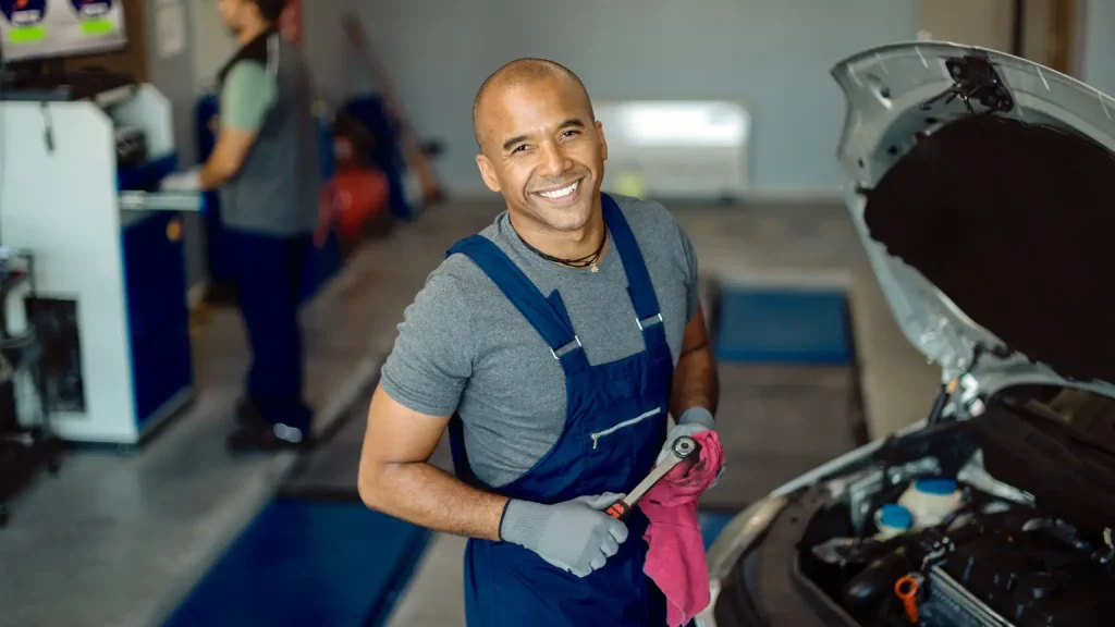 Transmission diagnostic tools being used by a smiling mechanic in a workshop while inspecting a car engine