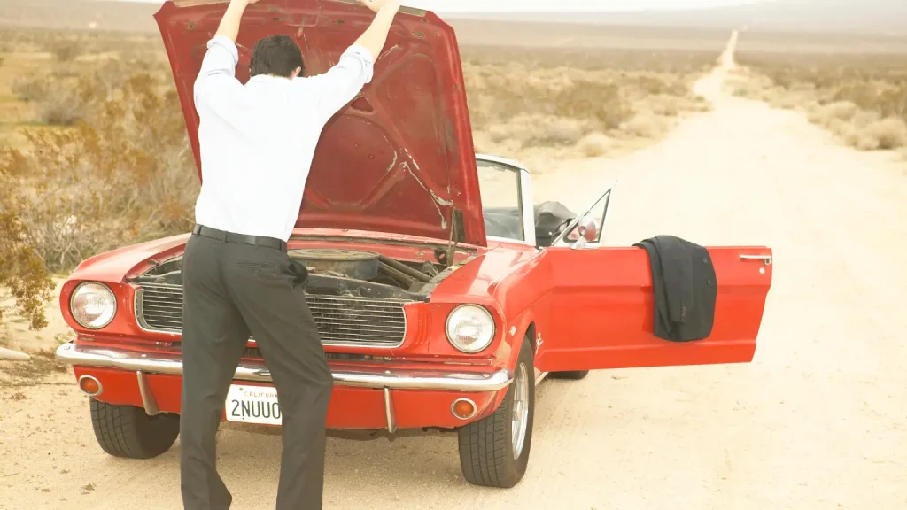 Man inspecting the engine of a vintage red convertible on a deserted road