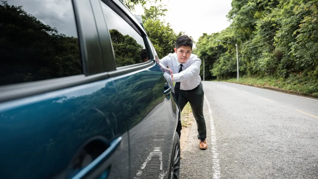 Quick transmission repair in need for a man in business attire that pushes a broken-down car on the side of the road